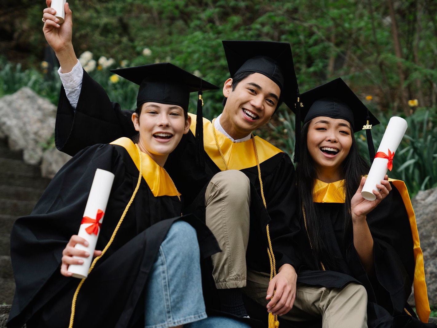 Three joyful graduates in caps and gowns holding their diplomas