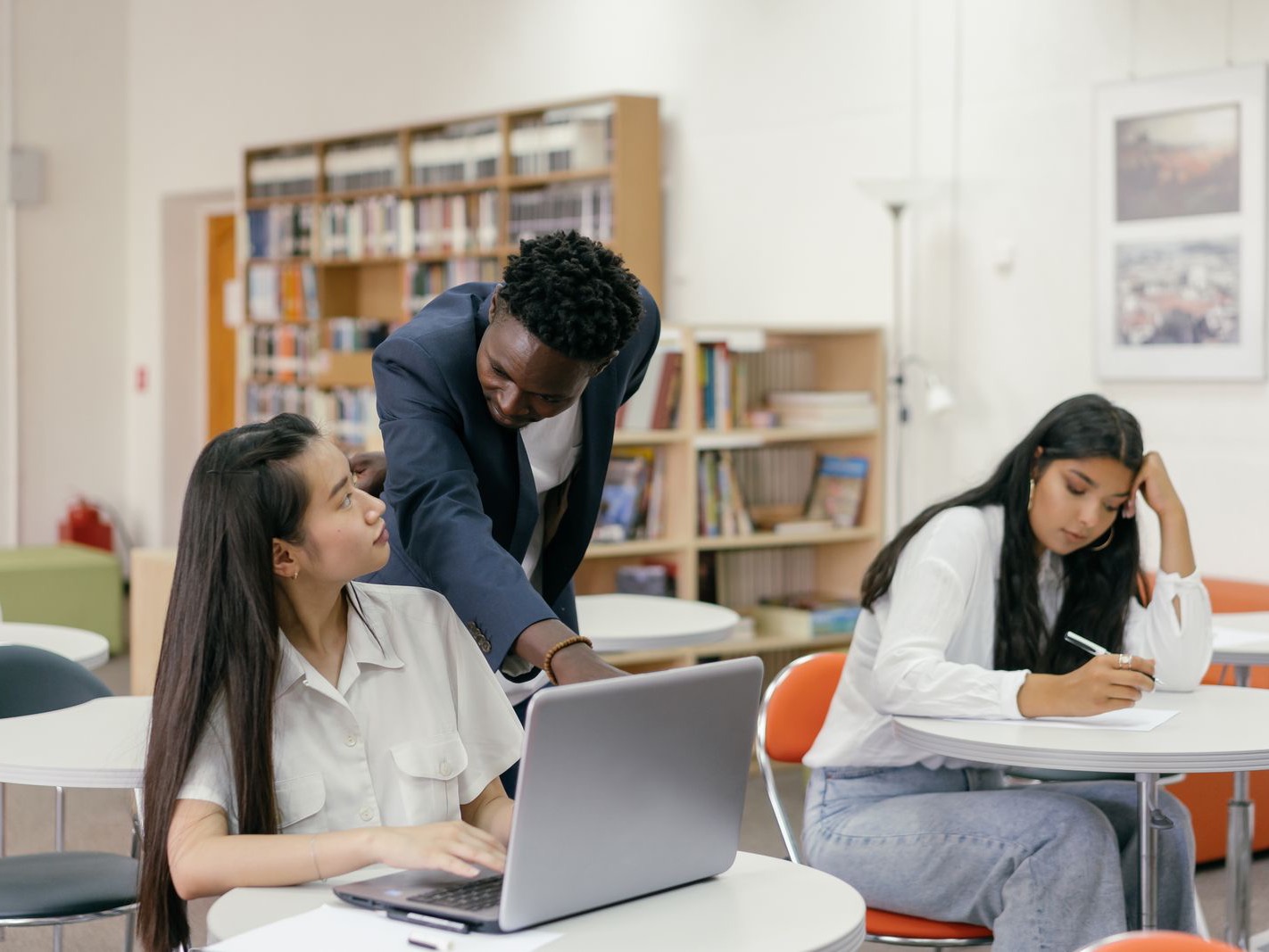 A tutor helping a student at a laptop in a library study space