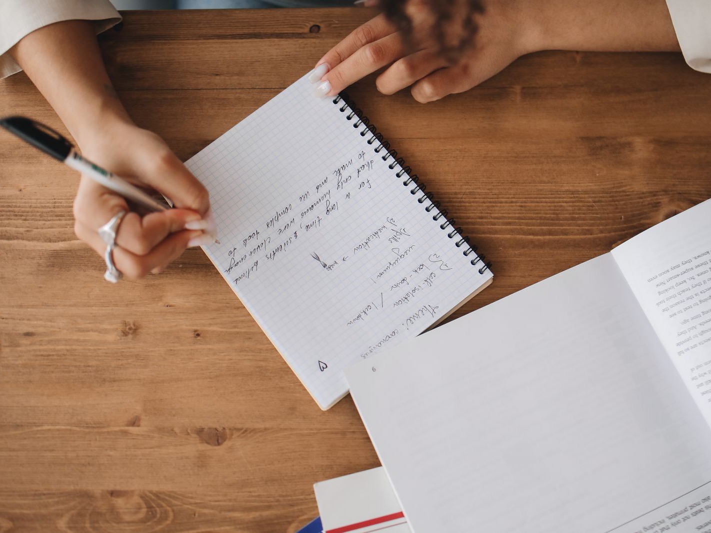 Close-up of a student writing notes in a notebook beside an open book